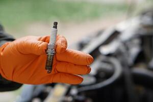 Close up mechanic hands hold old spark plug, spare part of car engine. Concept, machine maintenance, fix, repair, check or diagnose automobile problems by engine specialist. photo