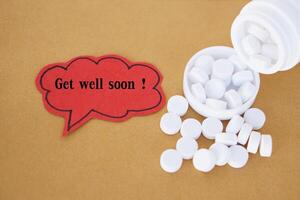 Red paper card, bubble speech with text Get well soon.  Blurred white pills medicines. Concept, health care. Words for encouragement to recover for illness, sick. Greeting card. photo