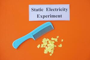 Comb and small pieces of paper. Equipment, prepared to do experiment about static electricity. Orange background. Concept, Science lesson, fun and easy experiment. Education. Teaching aids. photo