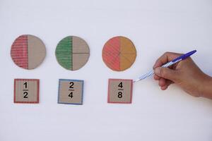 matemáticas enseñando materiales acerca de fracción. mano sostener bolígrafo a punto a circulo papel a espectáculo partes de color separación. concepto, educación. bricolaje arte como enseñando ayuda en matemáticas sujeto. foto