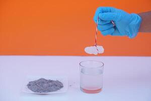 Hand wears blue glove hold alum stone to do science experiment  on glass of water and tray of ash about sedimentation by using alum stone with ash water in glass.Concept, Education, Science lesson. photo