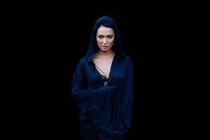 Young beautiful woman with a black hair and in the dark blue cloak with hood at the black background photo