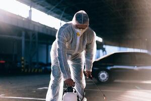 Man dressed white protective overalls spraying surface antibacterial sanitizer sprayer during quarantine photo