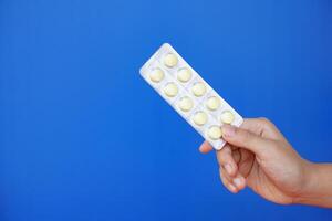 Close up hand holds blister pack of medicine pills. Blue background. Concept, pharmacy, medical treatment and health care, use under doctor prescription of illness symptoms. photo