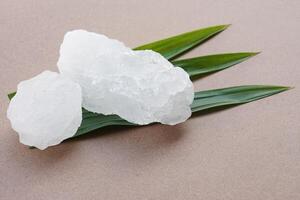 White crystal alum stones or Potassium alum on green leaves. Chemical compound. Useful for beauty and spa treatment. Use to treat body odor under the armpits as deodorant and make water clear. photo