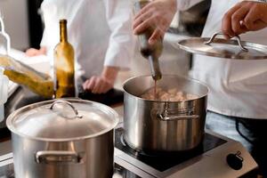 Closeup hands of chef pouring wine into pot with meat. In the background is a blurred figure of another chef photo