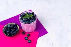 Tasty fresh blueberry yoghurt shake dessert in glass standing on white table purple napkin background. photo