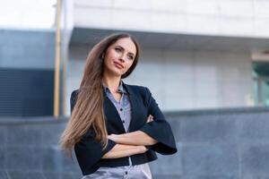 Business woman with long hair dressed black jacket standing outdoor near corporate office building hands folded photo