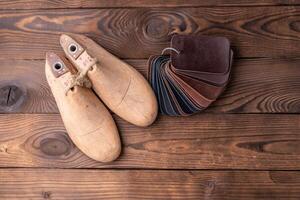 Leather samples for shoes and wooden shoe last on dark wooden table. photo