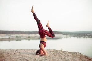 An attractive young woman doing a yoga pose for balance and stretching near the lake high in the mountains photo