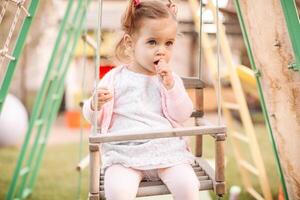Funny little child, adorable preschooler girl in pretty dress having fun on a swing in the park on summer day photo