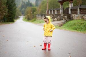 Playful girl wearing yellow raincoat while jumping in puddle during rainfall photo