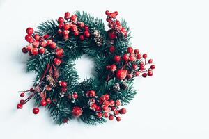 Christmas decorative wreath of holly, ivy, mistletoe, cedar and leyland leaf sprigs with red berries over white background. photo