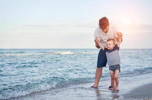 joven caucásico papá con pequeño hijo caminar calentar verano día a lo largo el mar costa. verano familia vacaciones concepto. amistad padre y hijo. foto