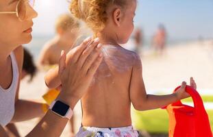 Caring mother apply sunblock to the back of her little daughter. Summer vacation sea beach photo