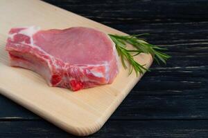 Top view of one pieces raw pork chop steaks with rosemary on a cutting board. photo