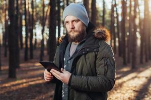 cerca arriba retrato de adulto masculino caminante utilizando digital lengüeta y mirando para ubicación durante caminata en naturaleza. hombre en caminata utilizando digital tableta para navegación. foto