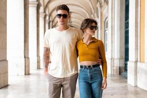 Young beautiful hipster couple in sunglasses in love walking on old city street photo