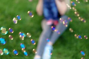 Unfocused unrecognizable mother inflates soap bubbles with her little son in a park on a sunny summer day. focus on the bubbles photo