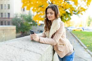 Beautiful caucasian brunette girl standing warm autumn day with background of trees with yellow foliage and a city. Dressed wool sweater and jacket. photo