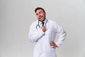 Young handsome modern doctor in a white medical gown stands in the studio on a white background. Student trainee of a medical university. photo