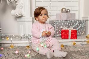 Beautiful cute little girl sitting on the floor near the New Year tree. Holiday mood, childlike spontaneity and sweet atmosphere photo