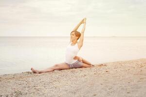 Beautiful girl practicing yoga on the beach near the sea. Sits on a twine, does a stretching. photo