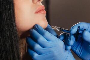 Closeup of young woman receiving injection in beauty salon. Cosmetology. Filler injection chin make chin longer photo