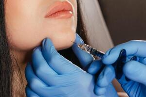 Closeup of young woman receiving injection in beauty salon. Cosmetology. Filler injection chin make chin longer photo