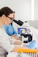 Medical Research Scientist Looks at Biological Samples Under Digital Microscope in Applied Science Laboratory. Beautiful Caucasian Lab Engineer in White Coat Working on Vaccine and Medicine photo