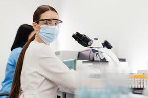 Medical Research Scientist Looks at Biological Samples Under Digital Microscope in Applied Science Laboratory. Beautiful Caucasian Lab Engineer in White Coat Working on Vaccine and Medicine photo