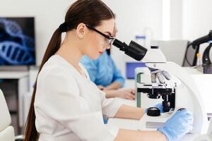 Medical Research Scientist Looks at Biological Samples Under Digital Microscope in Applied Science Laboratory. Beautiful Caucasian Lab Engineer in White Coat Working on Vaccine and Medicine photo