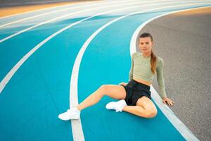Tired happy woman runner taking rest after run sitting running track photo
