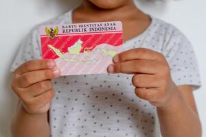 Jacarta, Indonesia, 2024 - un pequeño niña en blanco vestir participación el indonesio niño identidad tarjeta o kartu identitas anak foto