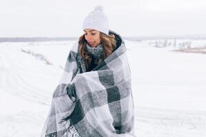 beautiful caucasian blonde girl in a white woolen hat covered by a warm blanket photo