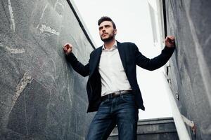 handsome young businessman with a beard and in a business suit standing on the street against the background of the office building photo