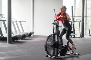 Woman exercise bike gym cycling training fitness. Fitness male using air bike cardio workout. photo