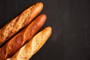 Three crispy french baguettes lie on an old wooden table with free space for text photo