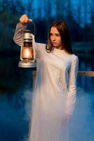 Mysterious mystical girl in a dark night forest with a kerosene lamp in her hands photo