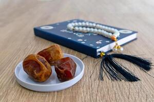 View of a plate of dates fruit on the wooden table with a small book and prayer beads photo