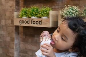 An Asian little girl with curly hair enjoying a chocolate ice cream in the cafe photo