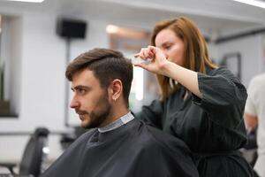 hermoso azul ojos hombre sentado en Barbero tienda. estilista peluquero mujer corte su cabello. hembra Barbero. foto