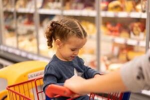 pequeño niña se sienta compras carretilla cerca tiendas foto