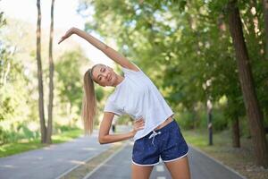 Woman runner stretching arms before exercising summer park  morning photo