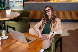 negocio mujer restaurante propietario utilizar ordenador portátil vestido elegante traje pantalón sentado mesa en restaurante con bar mostrador antecedentes foto