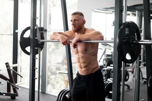 Gym man leaning barbell resting after hard training. Handsome caucasian athlete take break. photo