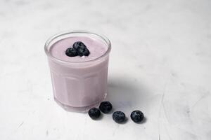 Tasty fresh blueberry yoghurt shake dessert in glass standing on white table background. photo