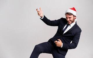 Young handsome caucasian guy in business suit and Santa hats stands on white background in studio and Plays on an imaginary guitar. photo