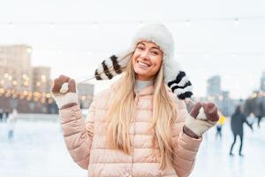 hermosa encantador de edad mediana niña rubia pelo calentar invierno chaquetas de punto guante soportes hielo pista antecedentes pueblo cuadrado. Navidad estado animico estilo de vida foto