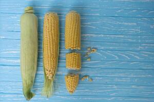 Corn cob with green leaves lies on table blue color background. photo